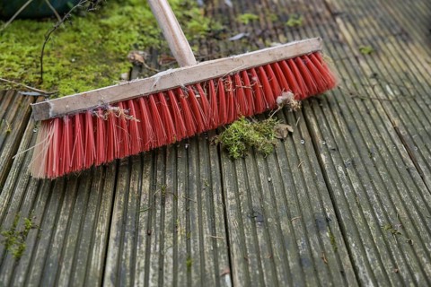 Outdoor broom with red plastic bristles on a weathered wooden deck with slippery algae and moss,