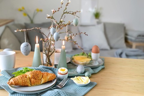 Breakfast table with boiled egg, croissant and pastel turquoise Easter decoration in a small living
