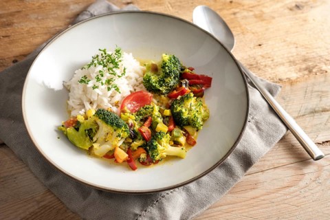 Vegetarian broccoli curry with rice and parsley garnish in a gray plate on a rustic wooden table,