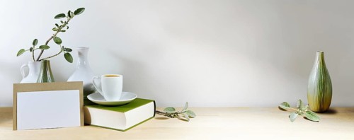 Mock-up of a blank greeting card, vases with sage leaf branch and coffee cup on a book, wooden