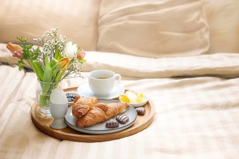 Romantic breakfast in bed with flowers, croissant, coffee cup and hearts from chocolate on beige