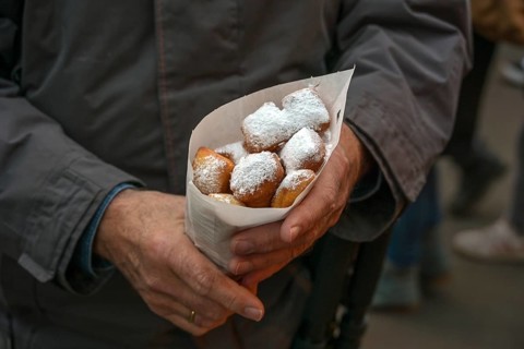 Man holding a paper bag of Mutzenmandeln, deep fried shortcrust dough pastry with almonds covered