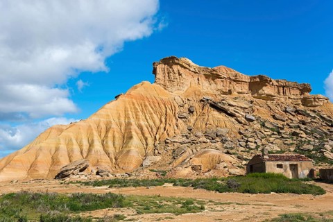 Small hut in front of a striking rocky hill in a desert-like landscape under a blue sky, Bardenas