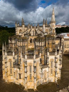 An imposing Gothic cathedral with several towers and a detailed façade under a cloudy sky, aerial