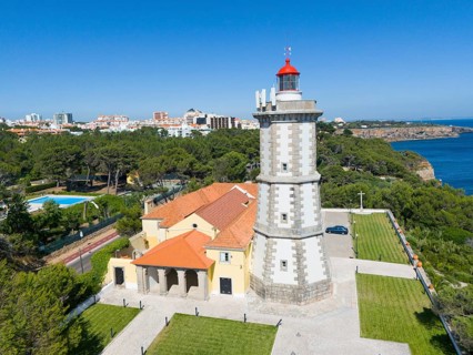 A lighthouse with a red top next to a building with a view of the forest and the sea, aerial view,