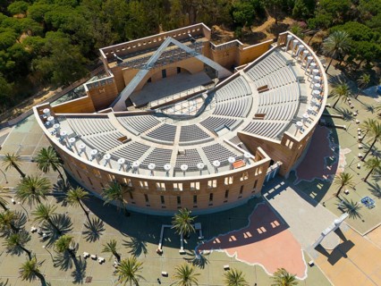 An auditorium surrounded by trees and palm trees, showing ancient Roman architecture with large
