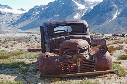 Old, rusty car in a junkyard with a view of mountains and blue sky in the background, remains from