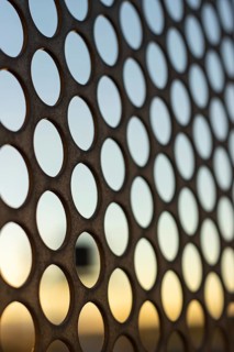 Vertical view of the sunset through a perforated steel sheet with holes in the shape of circles.