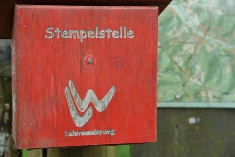 Red stamping point with hiking sign on the Lahnwanderweg trail at the source of the Lahn with