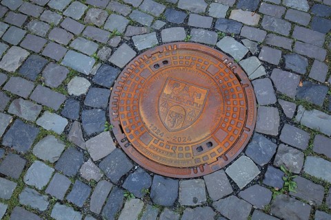 Round rusty manhole cover with city coat of arms and inscription university town, year, round,