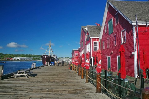 Harbour with red buildings and a boat on the water along a wooden jetty under a blue sky, fishing,