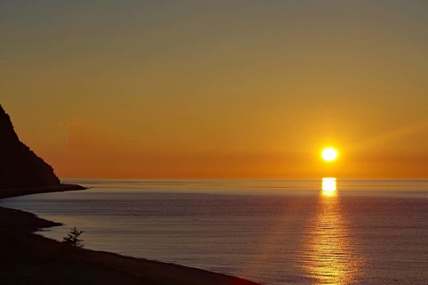 Sunset over the calm sea with a coastline and clear sky in the background, St. Lawrence River,