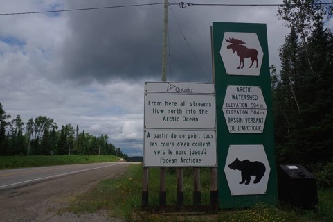 Road sign and traffic signs in a rural wooded area on a cloudy day, watershed, Manitoba, Canada,