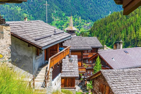 Interlocking old wooden houses with wooden shingle roofs, Saint Theodule church at the back,
