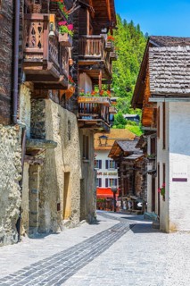 Paved footpath surrounded by old wooden houses, flower boxes on balconies and windows, historic
