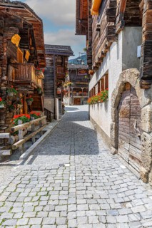 Paved footpath surrounded by old wooden houses, flower boxes on balconies and windows, historic