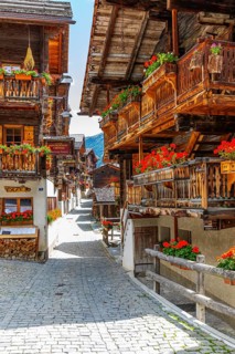Paved footpath surrounded by old wooden houses, flower boxes on balconies and windows, historic