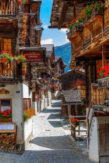 Paved footpath surrounded by old wooden houses, flower boxes on balconies and windows, historic