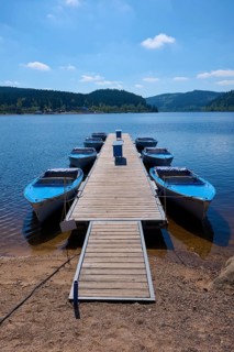 Jetty with moored boats on the Schluchsee, surrounded by mountains and forests, under blue sky,