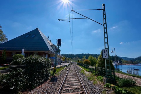 Railway tracks lead through a sunny landscape, surrounded by nature and the Schluchsee, railway