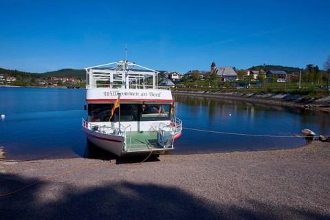 A boat with the inscription 'Welcome aboard' is anchored at the Schluchsee, in the background you
