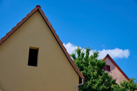 Two houses with gabled roofs, one beige and one pink, in front of a blue sky with scattered clouds