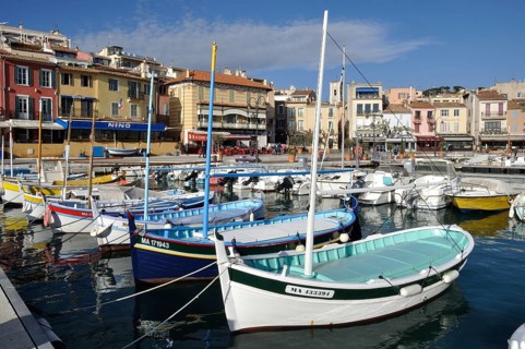 Colorful boats in a vibrant harbor with Mediterranean-style buildings under a clear blue sky,