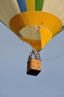 A colorful hot air balloon with a woven basket is soaring in a clear sky, Montgolfière in Charente