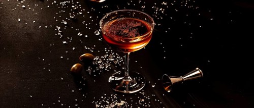 Sophisticated dark cocktail in a glass with a sugar rim, set in dim light creating elegant moody