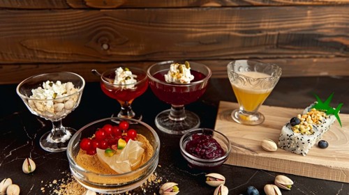 Variety of colorful desserts and cocktails on a wooden table with a sushi roll and elegant