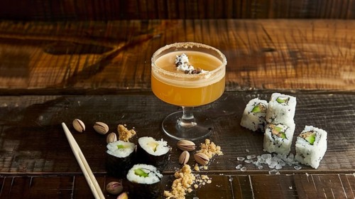 Orange cocktail and sushi rolls on a rustic wooden table, with pistachios and gourmet elements, AI