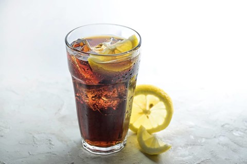 Fresh cola with ice cubes and lemon slices in a drinking glass, sweet caffeine drink against a