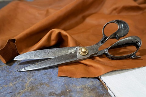 Big old scissors lying on a piece of leather in a craft workshop, copy space, selected focus,