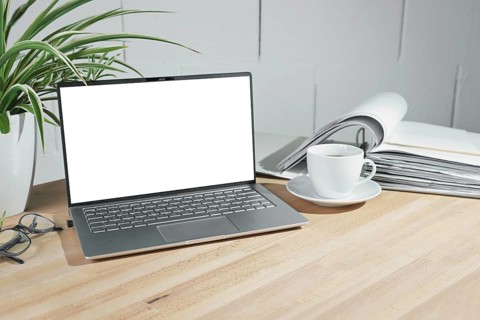 Mock up on an open laptop with a blank white screen, coffee cup and ring binder on a wooden office