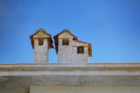 Light plastered chimneys with tiled roofs on a building in Greece, looking like little houses, blue