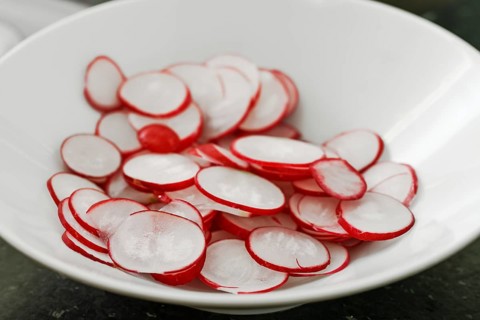 Slices of fresh raw radish in a white bowl, copy space, selected focus, narrow depth of field
