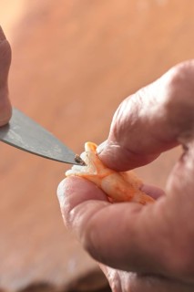 Hand holding a shrimp and removes the guts with a knife, preparation for cooking a seafood meal,