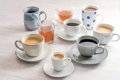 Group of different cups and mugs with coffee and tea drinks on a light table, selected focus,