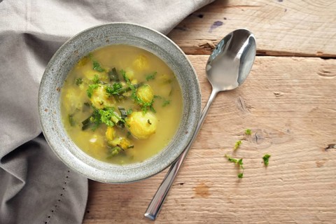 Vegetable soup with brussels sprout, leek and potato in a bowl, spoon and napkin on a rustic wooden