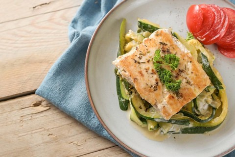 Roasted wild salmon fillet with parsley garnish on creamy zucchini vegetables and fresh tomato on a