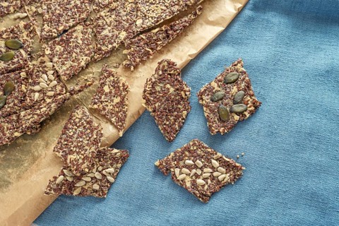 Crunchy whole grain snacks from oat and linseed topped with various seeds on baking paper and a