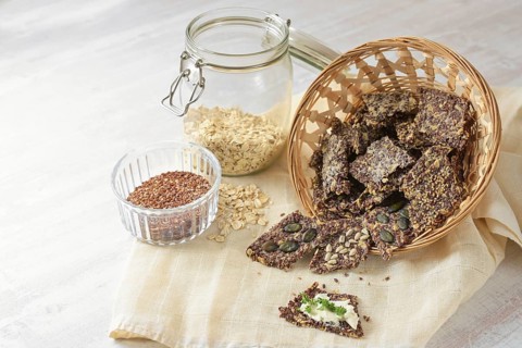 Crunchy snacks from linseed, oat flakes and various seeds in a basket, one with butter and parsley