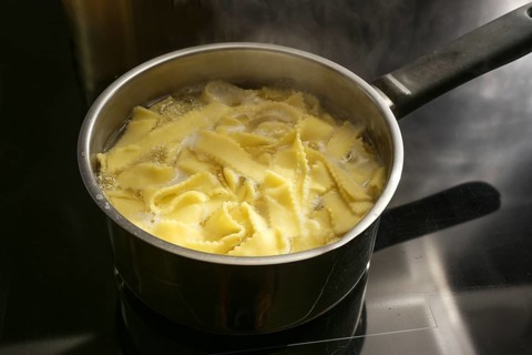 Pasta noodles are cooked in boiling water in a pot on a black stove top, preparing food concept,