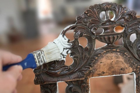 Painting an old chair made of dark decorated wood with a paint brush and white color to get a