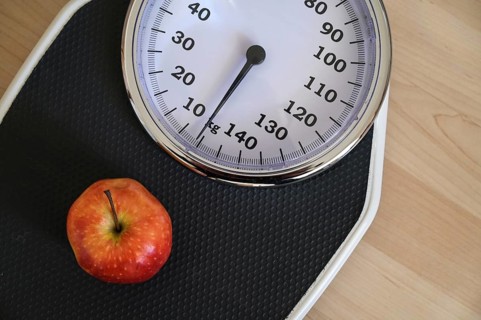 Red apple on an analogue personal scale on a wooden floor, concept for healthy eating, lose weight