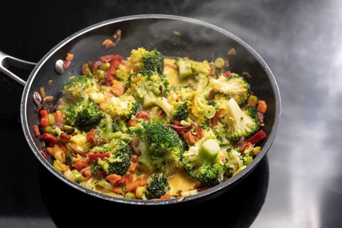 Vegetarian curry with broccoli and other vegetables in a steaming frying pan on a black stovetop,