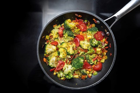 Stir-fried vegetable meal from broccoli, bell pepper, onion and tomato in a frying pan on the black
