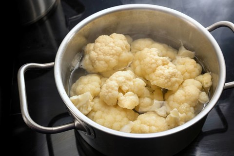 Cooking pieces of cauliflower in boiling water in a stainless steel pot on a black cooktop, healthy