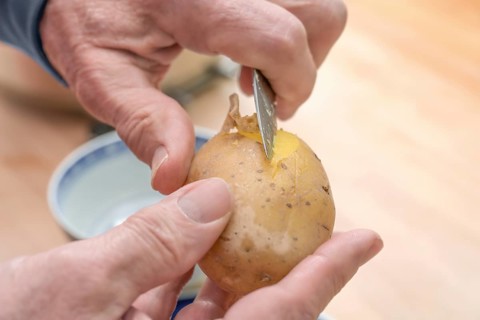 Hands of an elderly man peeling a cooked potato with a kitchen knife, preparing food, copy space,