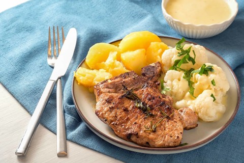 Dish with pork chop, cauliflower, potatoes and hollandaise sauce served with herb garnish on a